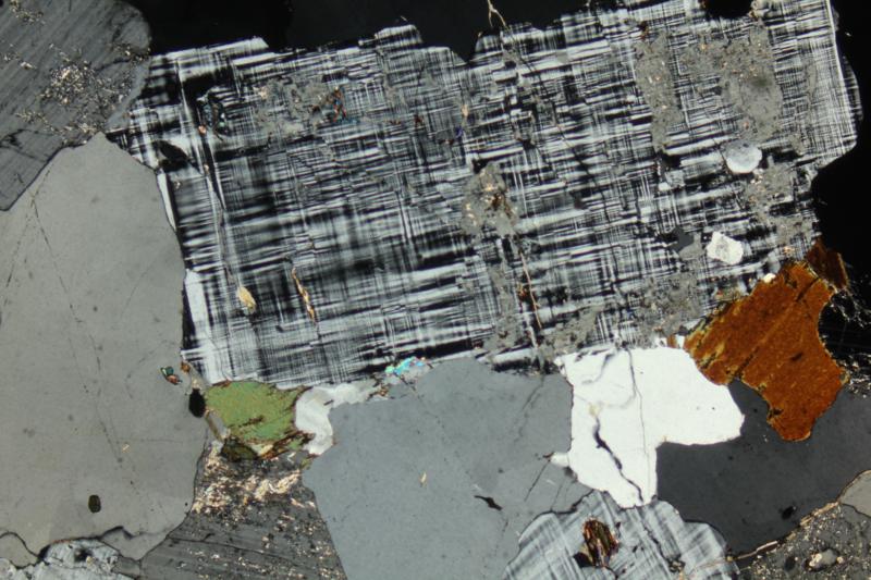 Microklien onder de microscoop in een matrix van andere mineralen. Microklien is te herkennen aan het gestreept 'tartan' patroon (collectie van Alex Strekeisen).